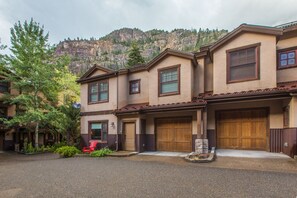 A row of two-story houses with brown roofs and beige walls, set against a mountainous backdrop.