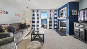 A living room with a sofa, coffee table, and a view of the outside. - 232 Edgewater | Lake Charlevoix Views | Downtown | Pool, Hot Tub, Sauna (Charlevoix)