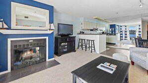 A modern living room with a fireplace, a television, and a dining area with a bar. - 232 Edgewater | Lake Charlevoix Views | Downtown | Pool, Hot Tub, Sauna (Charlevoix)