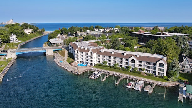 An aerial view of a waterfront hotel with a swimming pool, docked boats, and a bridge connecting to the mainland. - 233 Edgewater | Waterfront View | Pool, Hot Tub, Sauna | Sleeps 4 (Charlevoix)