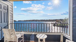 A balcony with a view of the water, a chair, and a small table. - 233 Edgewater | Waterfront View | Pool, Hot Tub, Sauna | Sleeps 4 (Charlevoix)
