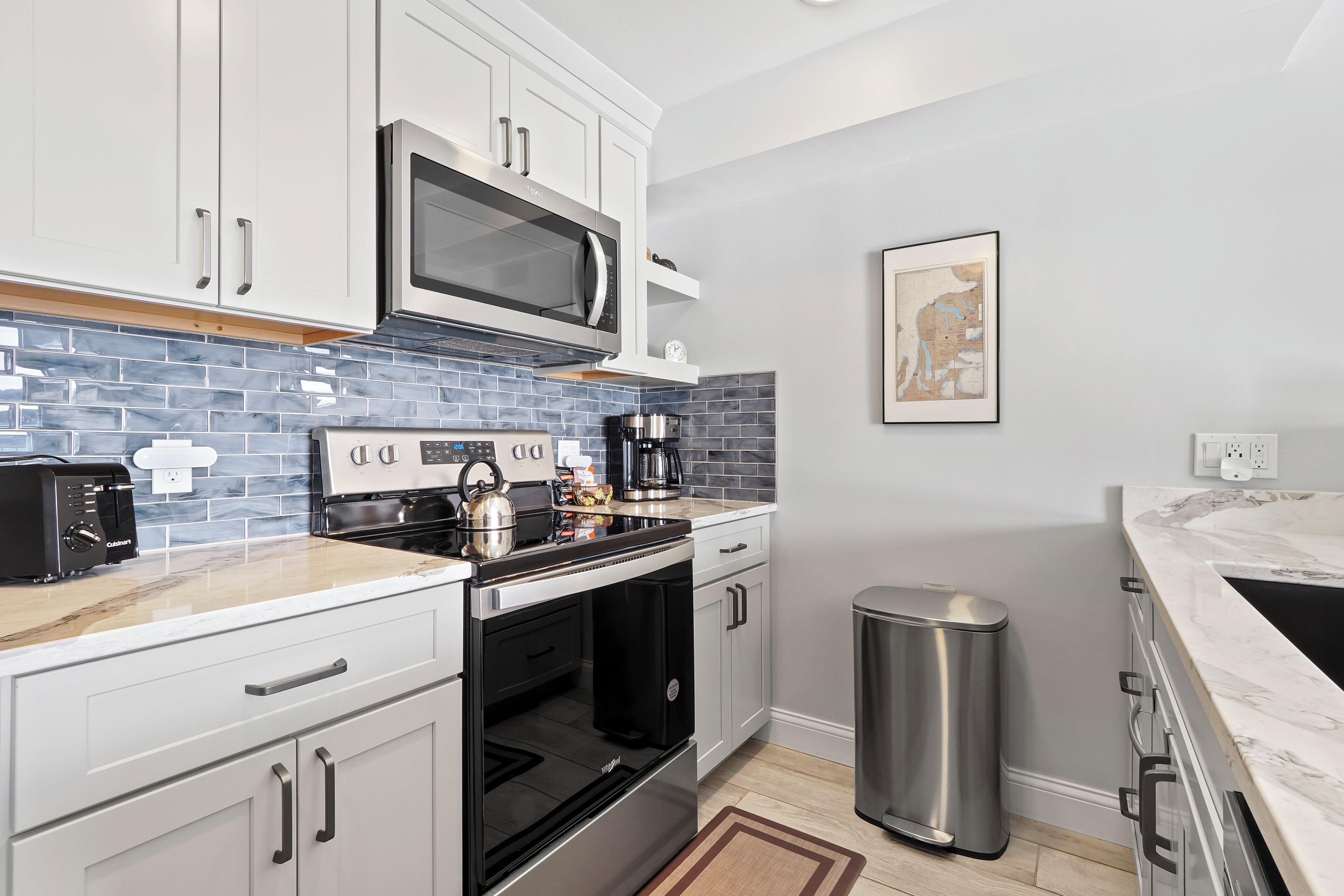 A modern kitchen with white cabinets, a stainless steel range, a microwave, and a coffee maker.