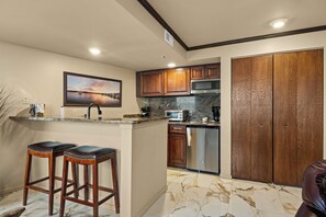 A kitchen with wooden cabinets, a built-in microwave, a stainless steel refrigerator, and a marble floor.