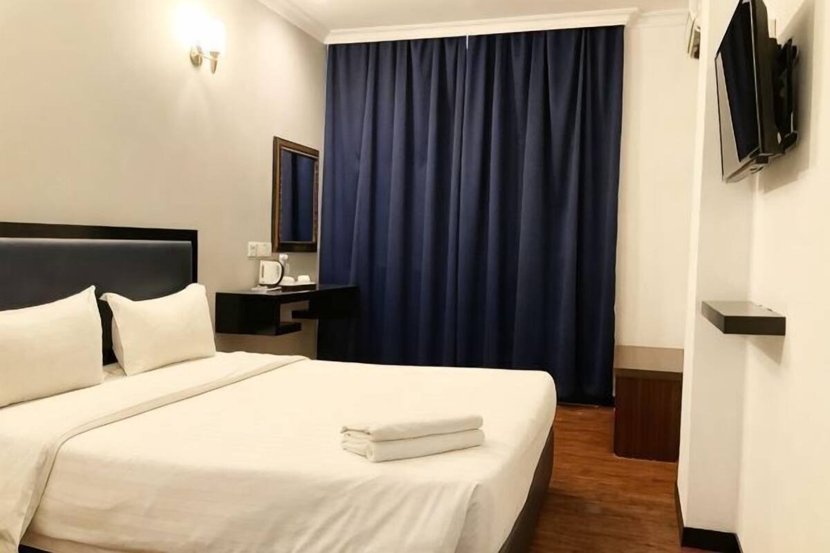 A hotel room with a bed, a nightstand, a TV, and a window with curtains.