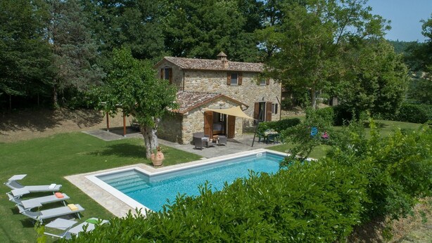 Une maison en pierre avec une piscine, du mobilier d’extérieur et un jardin.