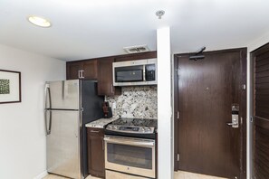 A compact kitchen with a refrigerator, microwave, oven, and a wooden door.