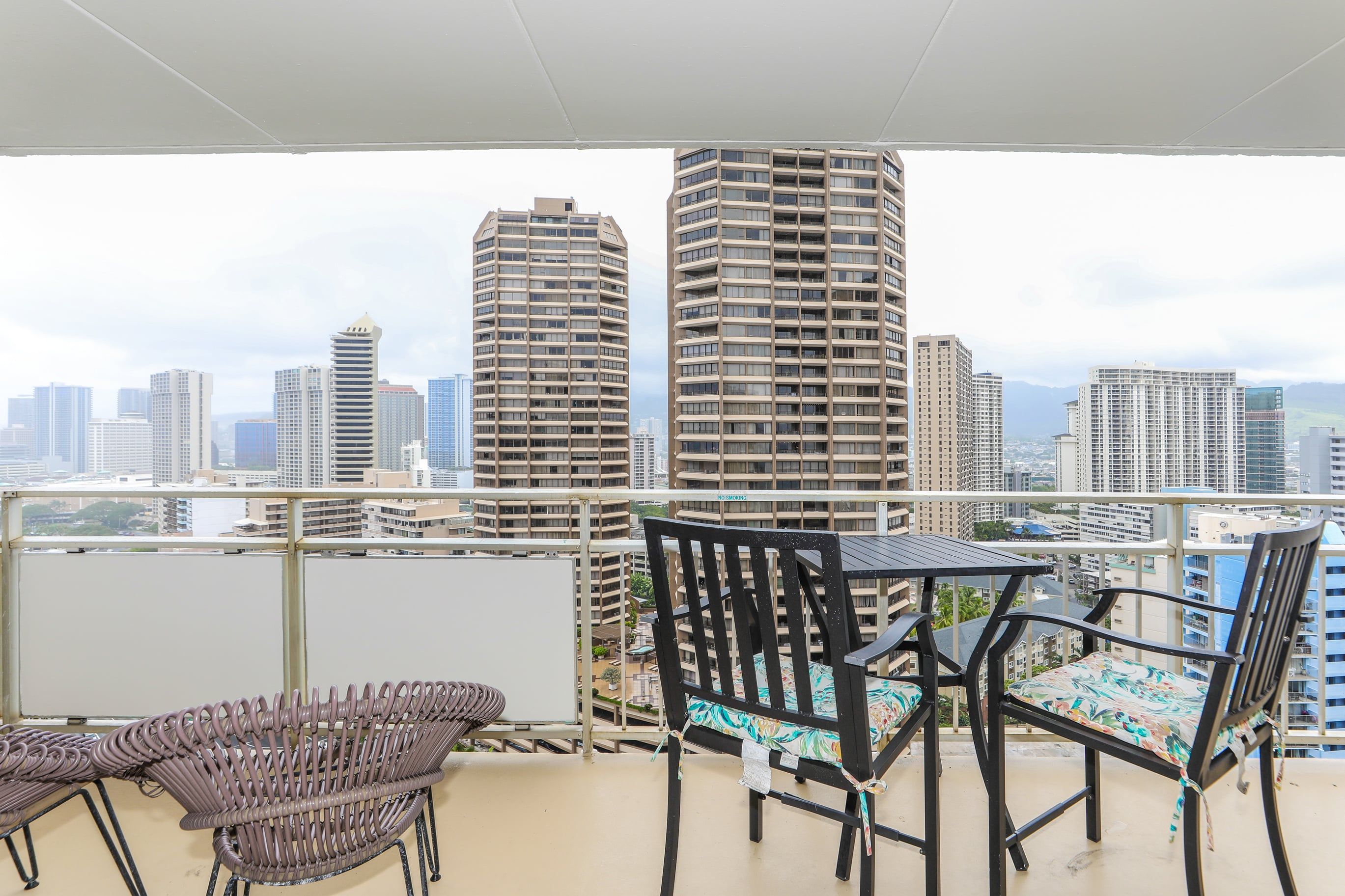 Un balcon avec vue sur la ville, comprenant une table et des chaises, ainsi qu’un panneau indiquant « INTERDICTION DE FUMER ».