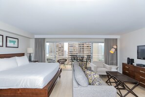 A hotel room with a large bed, a sofa, a TV, and a balcony with city views.