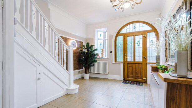 Un hall d’entrée spacieux avec un escalier en bois, une grande porte en arc de cercle et une plante en pot.