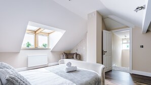 Une chambre avec un grand lit, un puits de lumière, un radiateur et une vue sur la pièce adjacente.