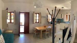 Una sala de estar con un sofá, una mesa de comedor con sillas, un área de cocina con armarios y una escalera.
