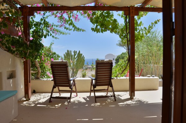 A covered outdoor seating area with two wooden chairs facing a view of the sea.