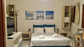 Una habitación de hotel con una cama, dos mesitas de noche, un televisor y un estante con artículos de tocador.