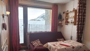 A cozy room with a bed, a small table, and a window overlooking a snowy landscape. - Cosy studio in Plagne Villages at the foot of the slopes (PLAGNE VILLAGE)