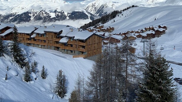 A snow-covered mountain resort with wooden buildings and ski slopes. - Cosy studio in Plagne Villages at the foot of the slopes (PLAGNE VILLAGE)