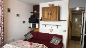 A cozy living room with a red sofa, a wooden cabinet, and a television. - Cosy studio in Plagne Villages at the foot of the slopes (PLAGNE VILLAGE)