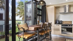 A modern kitchen with a dining area, large windows, and a view of greenery. - Marvellous Mount Apartment with pool, gym & beach (Mount Maunganui)