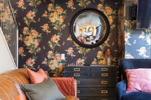 Een kamer met bloemenbehang, een spiegel, een dressoir met meerdere laden en een televisie.