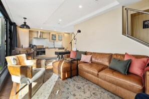 A modern living room with a leather sofa, a dining area, and a kitchen. - Marvellous Mount Apartment with pool, gym & beach (Mount Maunganui)