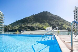 A swimming pool with a view of a mountain and modern buildings in the background.