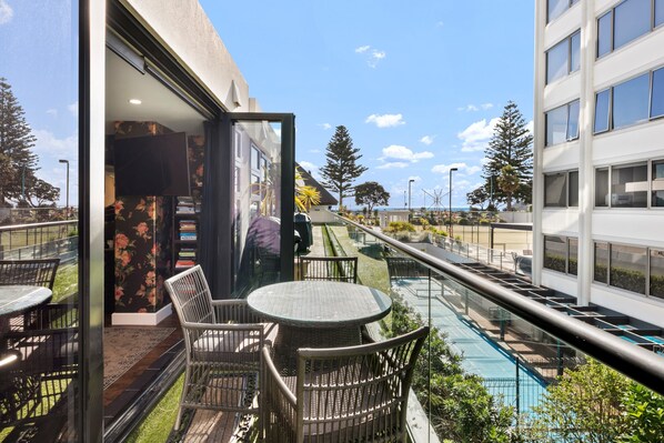 A balcony with outdoor seating, a pool, and a view of the surrounding buildings.