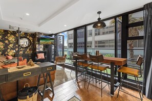 A modern living room with a sofa, a coffee table, and a dining area with chairs and a table. There is a large window with a view of the outside.
