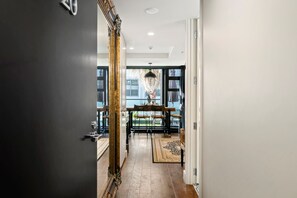 A hallway with a large mirror, a wooden door, and a view of a dining area with a table and chairs. - Marvellous Mount Apartment with pool, gym & beach (Mount Maunganui)