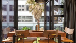 A dining area with a wooden table and four chairs, a potted plant, and a modern pendant light. - Marvellous Mount Apartment with pool, gym & beach (Mount Maunganui)