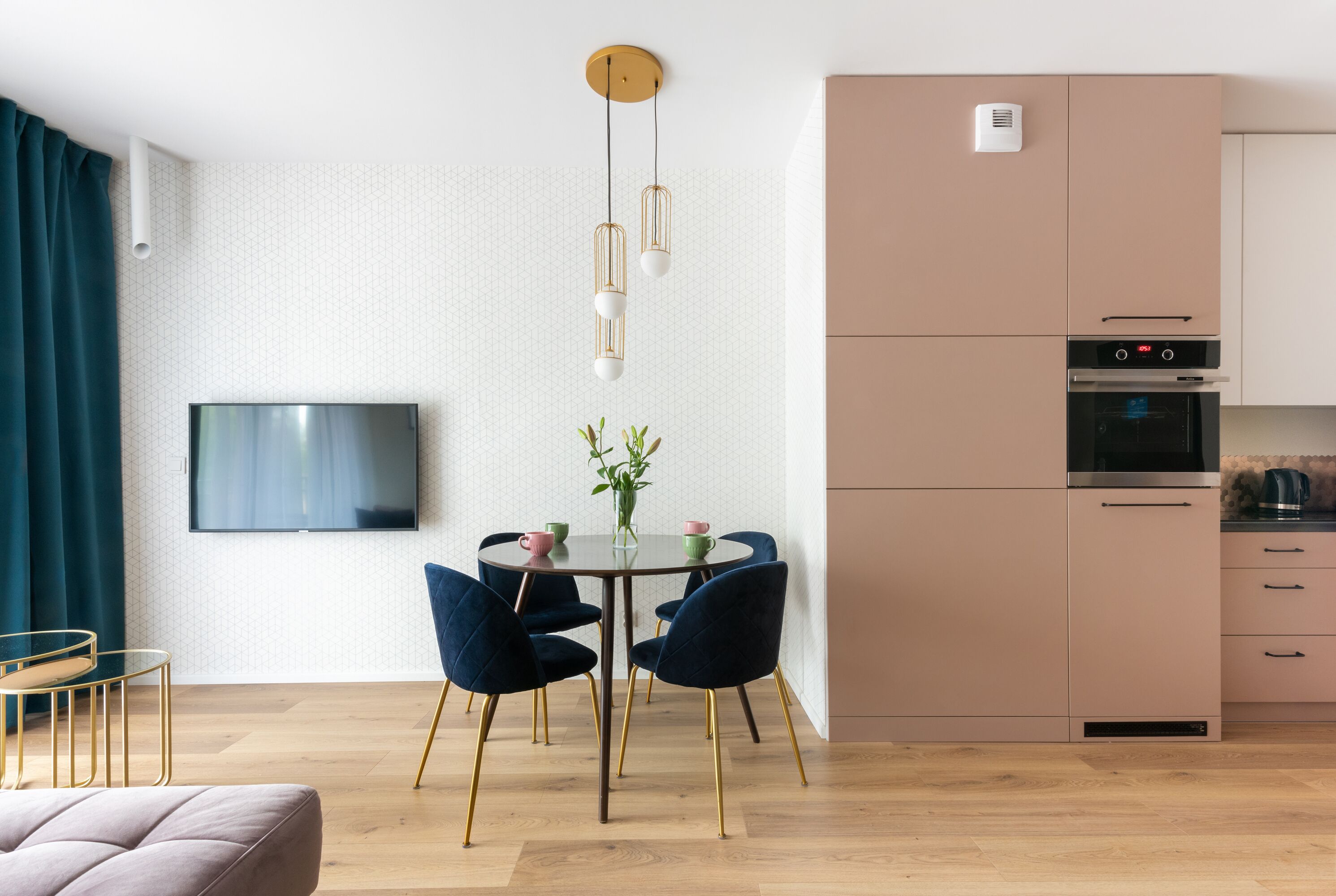 A modern kitchen with a built-in oven and microwave, a dining area with a round table and chairs, and a flat-screen TV mounted on the wall.