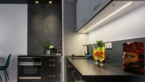 Una cocina moderna con armarios oscuros, horno integrado y una encimera con fruteros y un vaso de bebida.