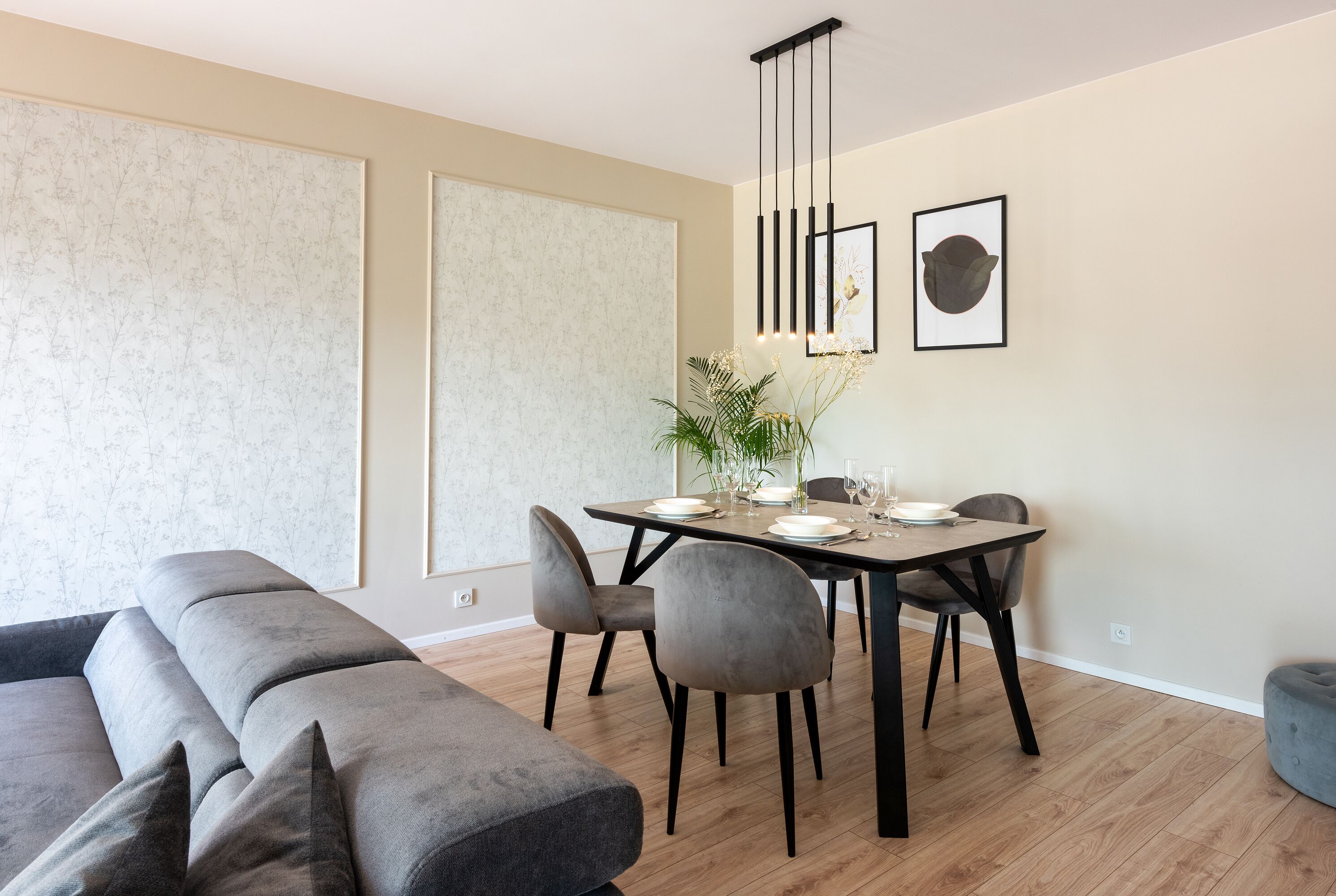 A modern dining area with a wooden table, grey upholstered chairs, and a hanging light fixture.