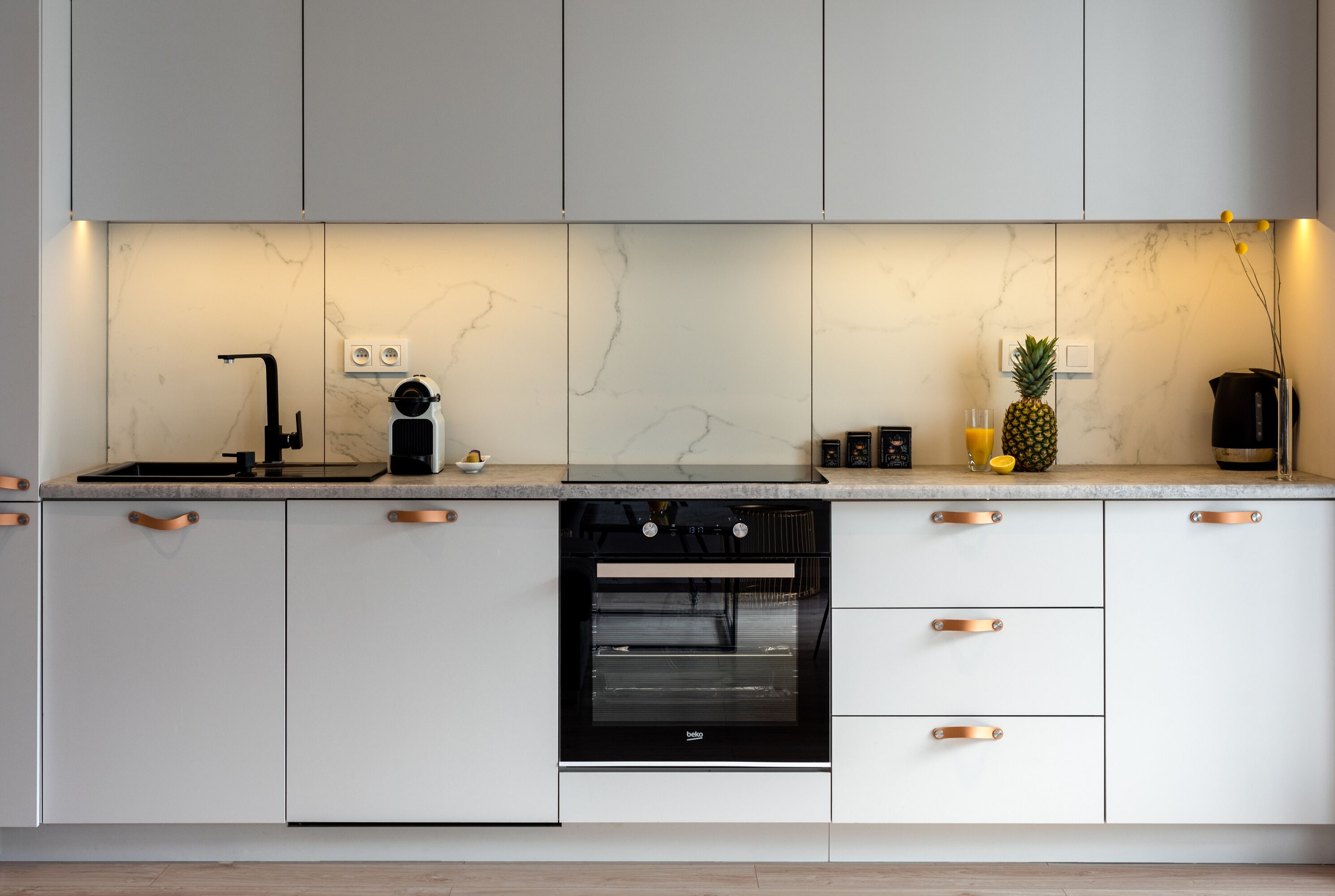 Eine moderne Küche mit weißen Schränken, einem schwarzen Backofen und einer Marmor-Spritzschutzwand.