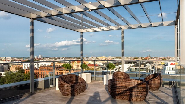Una terraza moderna en la azotea, con barandillas de vidrio, que ofrece una vista panorámica de la ciudad.