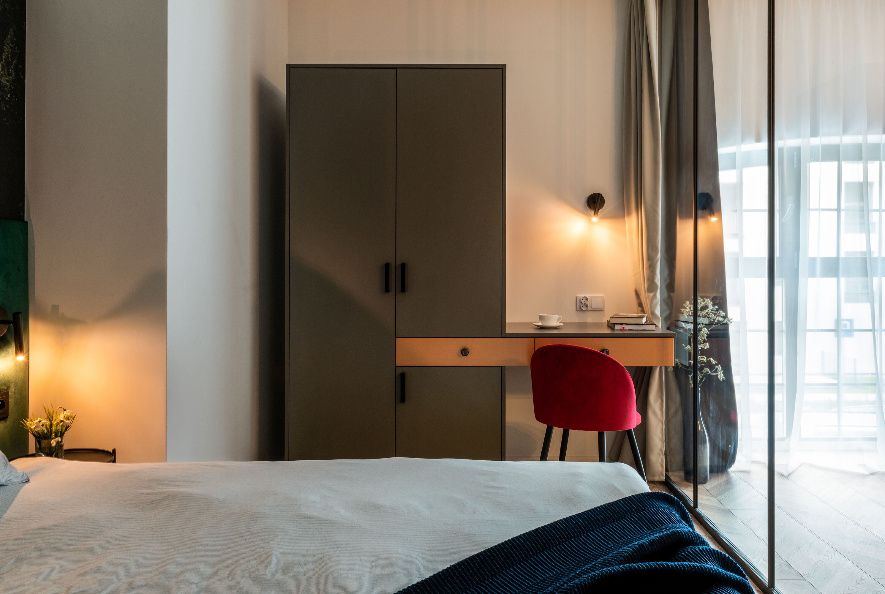 Une chambre d’hôtel comprenant un lit, un bureau avec une chaise, une armoire et une fenêtre avec des rideaux.