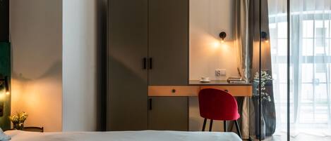 Une chambre d’hôtel comprenant un lit, un bureau avec une chaise, une armoire et une fenêtre avec des rideaux.
