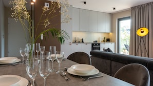 Un comedor moderno con una mesa dispuesta para seis personas, una cocina al fondo y un amplio ventanal con cortinas.