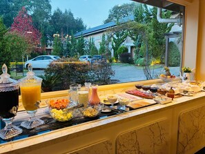 Un buffet de petit-déjeuner proposant une variété d’aliments et de boissons, avec vue sur un parking et des arbres, et un bâtiment en arrière-plan.
