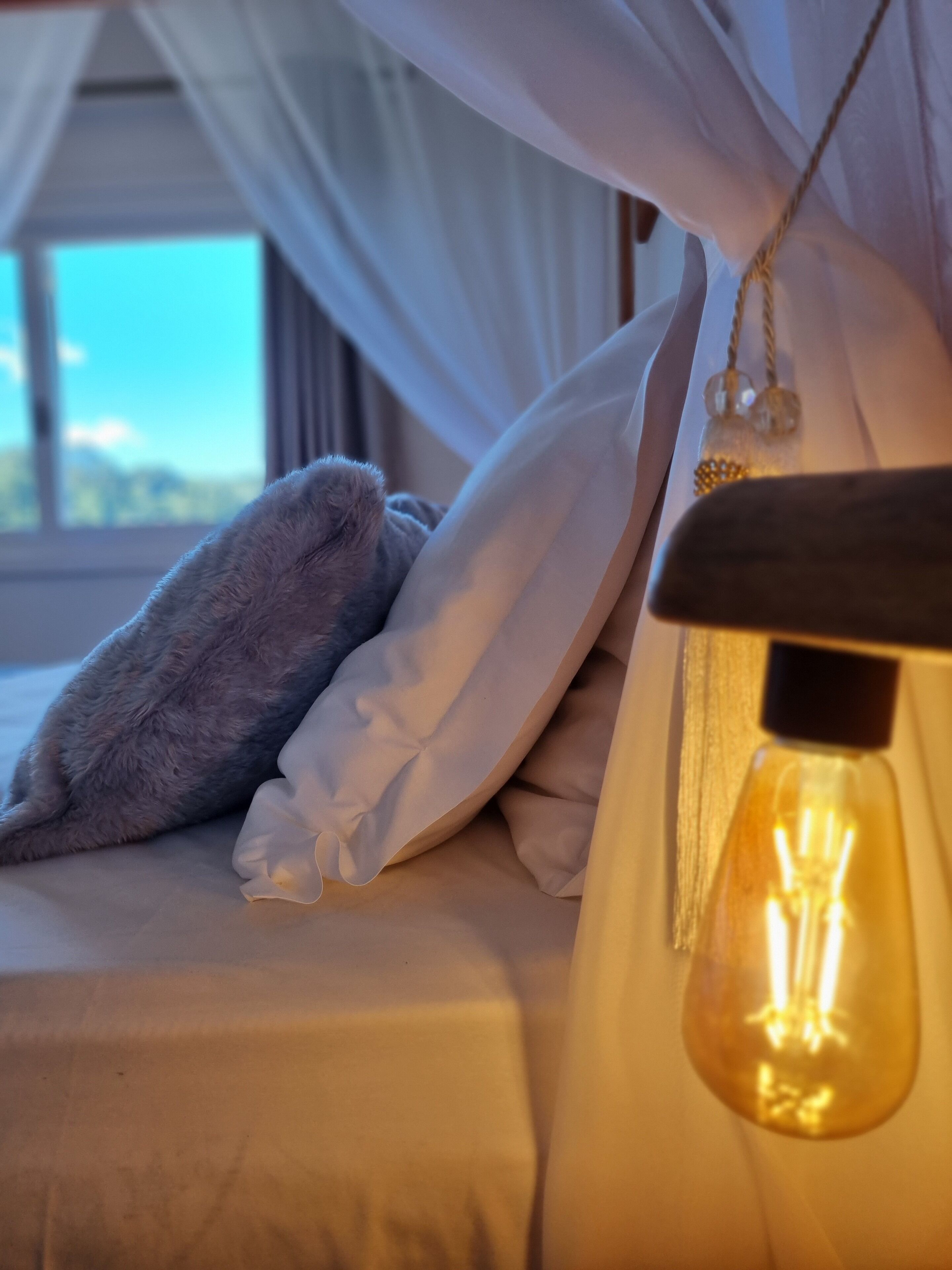 Una cama con ropa de cama blanca, un almohadón gris y un dosel blanco.
