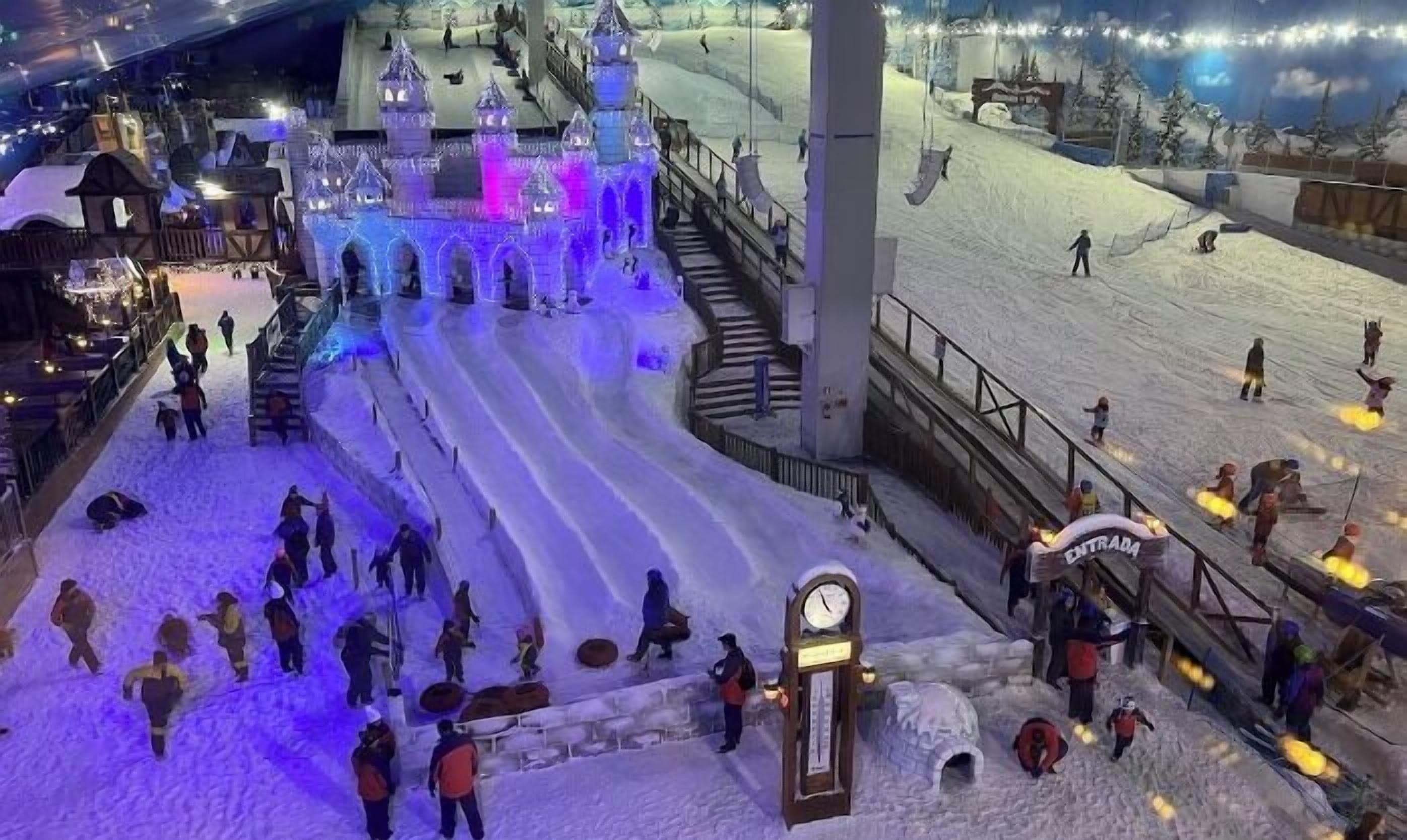 An indoor ski slope with artificial snow, a castle-like structure, and a clock.