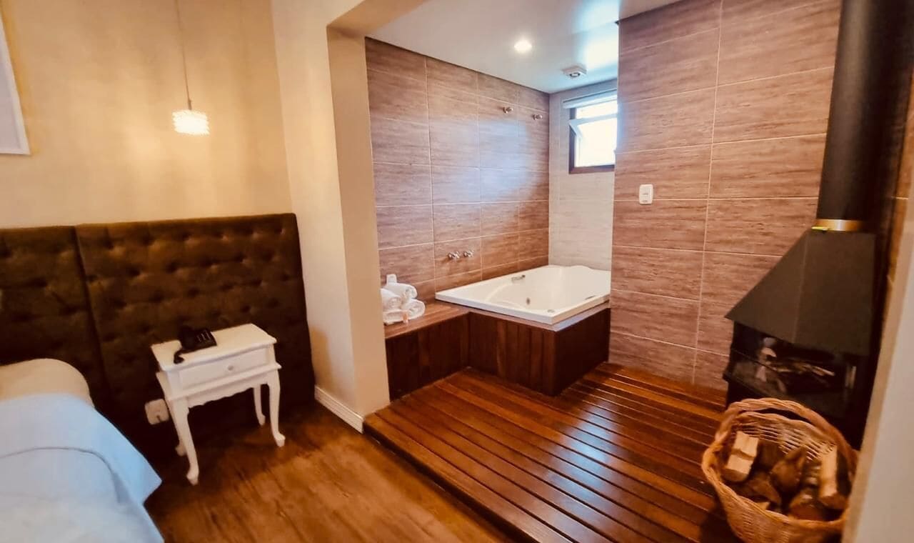 Un baño moderno con suelo de madera, una bañera grande, una mesita de noche blanca y un calentador negro.