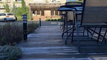 Eine Holzterrasse führt zu einem Gebäude mit einem braunen Dach und zahlreichen Fenstern.