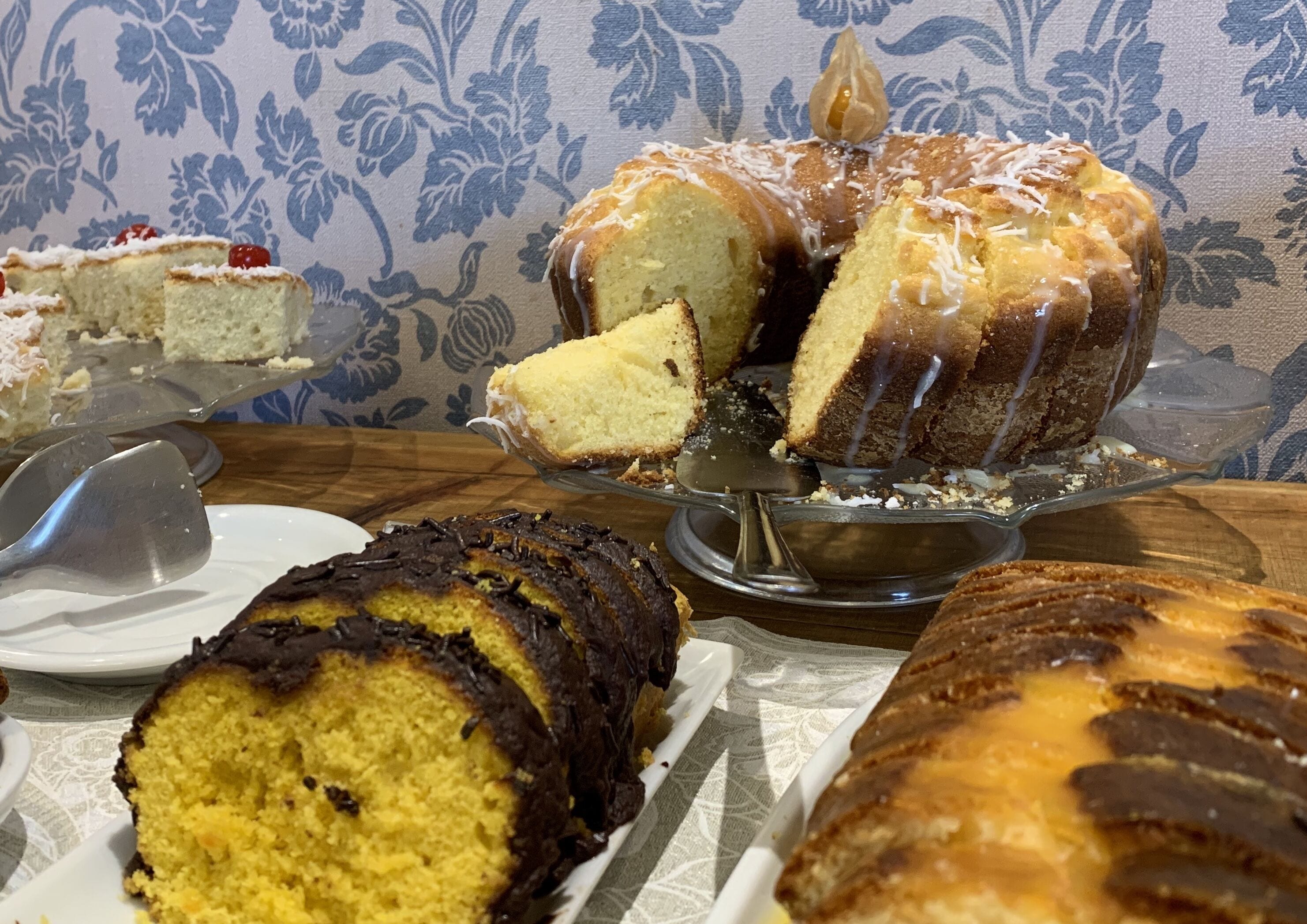 A variety of cakes on a table with a floral-patterned tablecloth.