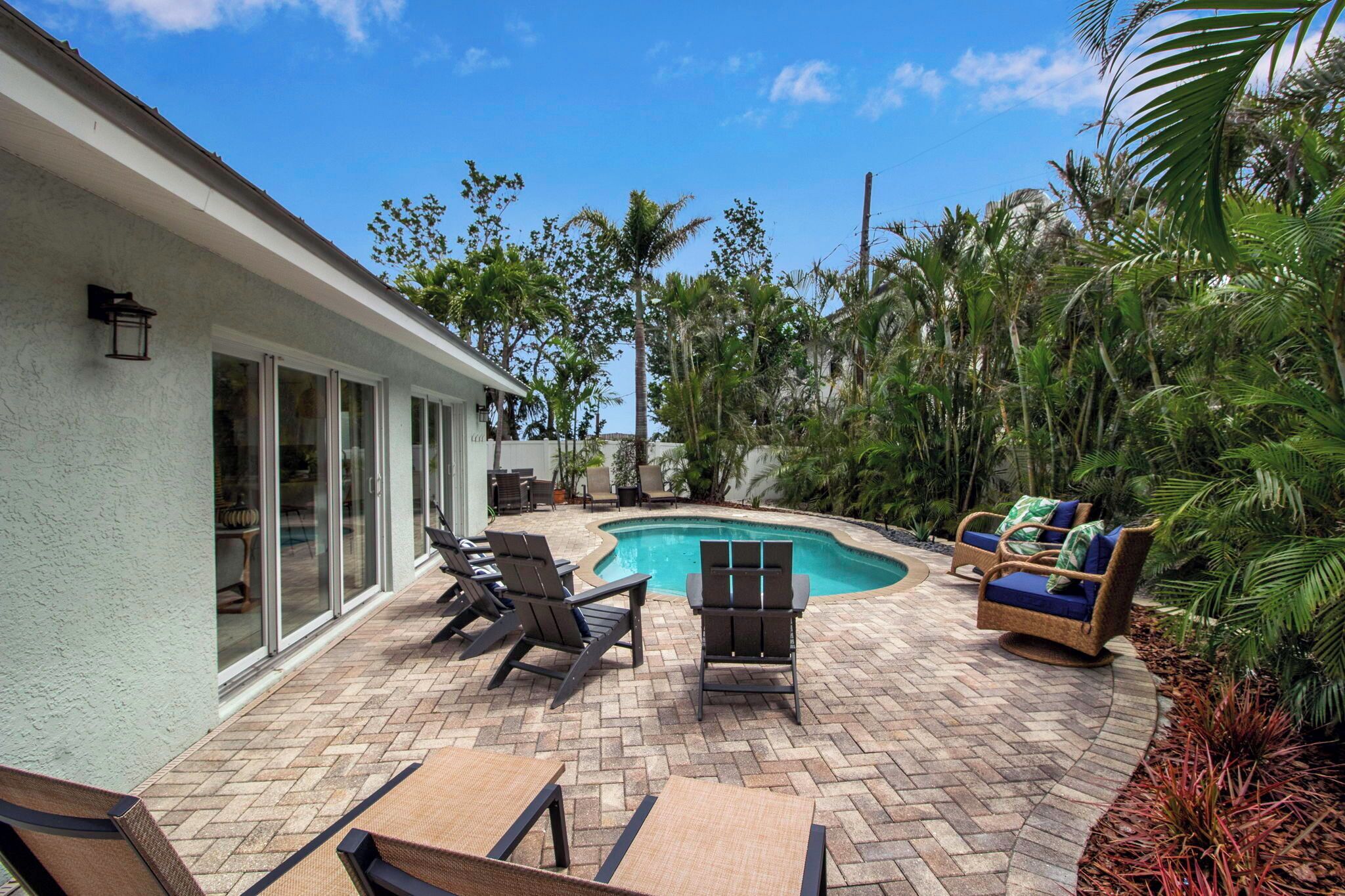 A backyard with a swimming pool, outdoor furniture, and tropical plants.
