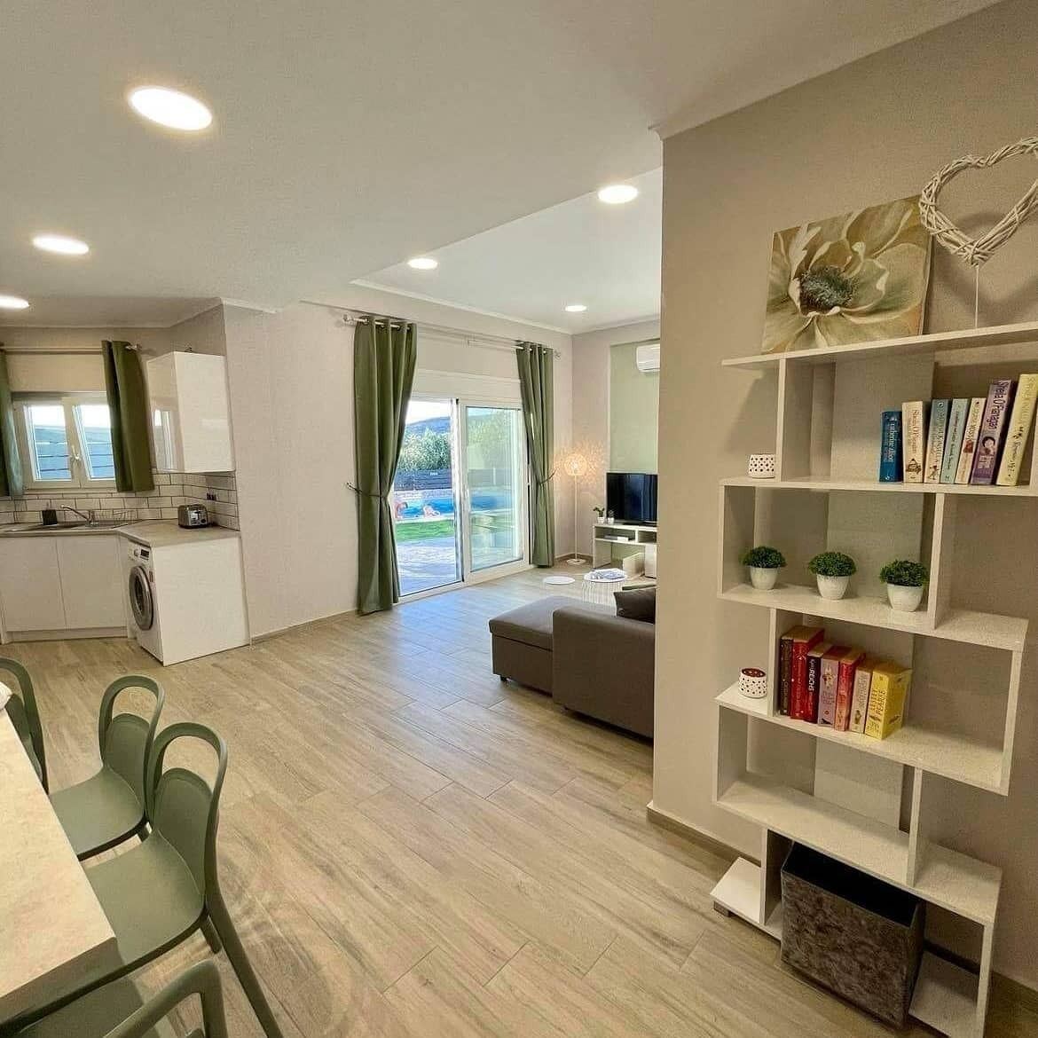 Eine moderne Wohnung mit Küche, Essbereich und Wohnzimmer. Es gibt ein Bücherregal, einen Fernseher und eine Schiebetür zum Außenbereich.