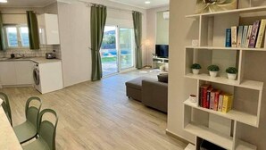A modern apartment with a kitchen, dining area, and living room. It includes a bookshelf, a TV, and a sliding glass door to the outside. - NEW Villa Sheila with private pool and BBQ. (Rethymno, Crete)