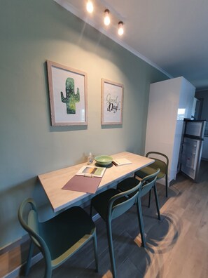 A dining area with a table, chairs, framed artwork, and a kitchen in the background. - NEW Villa Sheila with private pool and BBQ. (Rethymno, Crete)