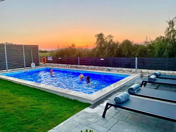 A rectangular swimming pool with a tiled edge, surrounded by a grassy area and a wooden fence. - NEW Villa Sheila with private pool and BBQ. (Rethymno, Crete)