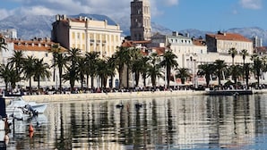 A waterfront promenade with palm trees, a historic tower, and buildings along the water's edge. - VillaTango (Okrug Gornji)