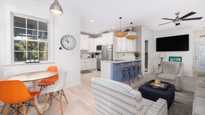 A modern kitchen with white cabinets, a built-in oven, and a dining area with a round table and orange chairs. - Prince's Folly! Walking Distance to Shops and Restaurants! (Folly Beach)