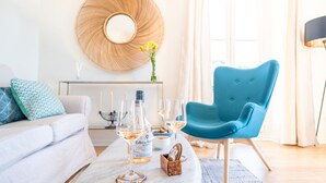 Un salon moderne avec un canapé, un fauteuil bleu, une table basse avec des verres et des bouteilles, et un élément décoratif mural.